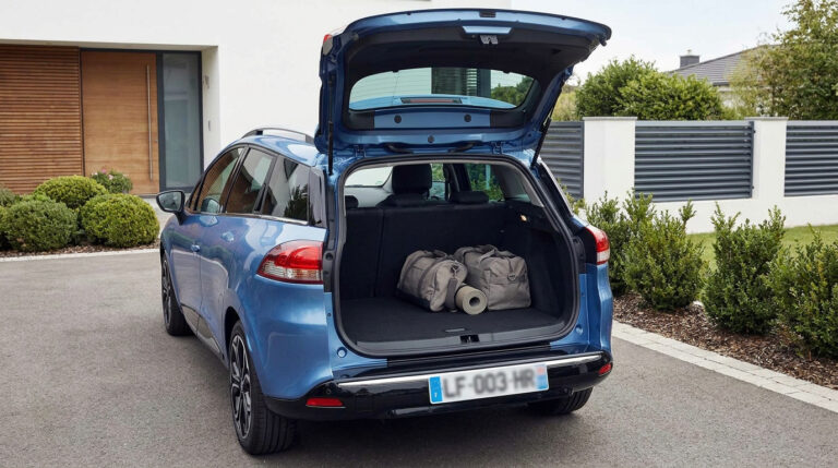 Renault Clio 4 Estate bleue avec le coffre ouvert contenant deux sacs de voyage, stationnée devant une maison moderne.