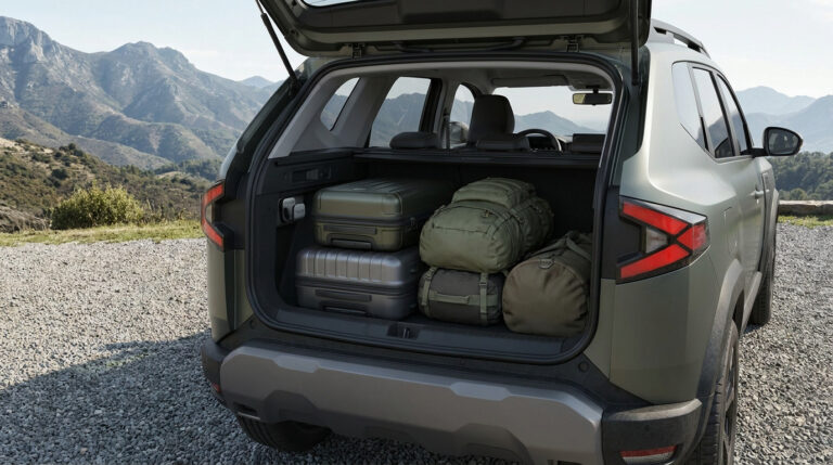 Coffre ouvert du Dacia Bigster vert olive chargé de bagages dans un paysage de montagnes.