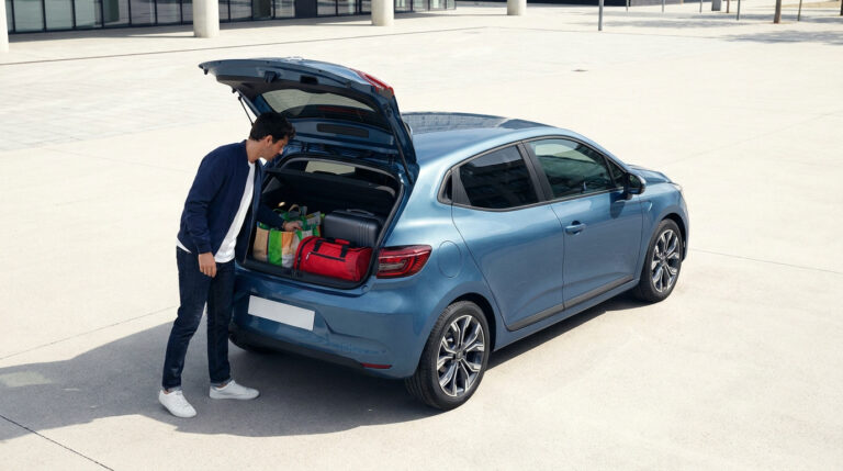 Un homme charge des sacs et une valise dans le coffre ouvert d'une Renault Clio 5 bleue sur un parking.